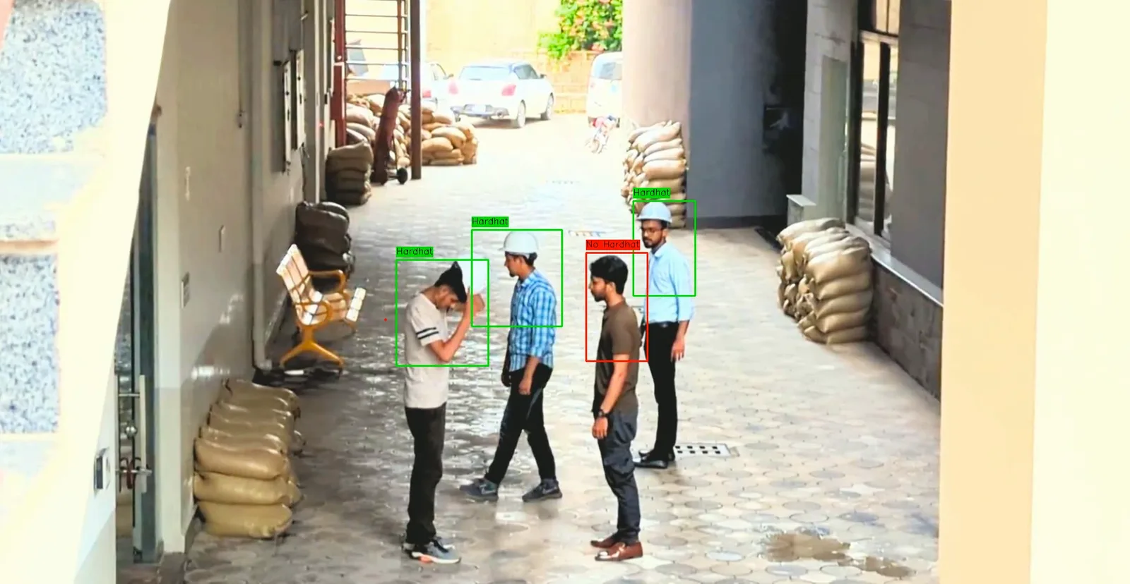 A fixed site camera looking down a walkway, with three workers boxed in green and labelled Hardhat and one boxed in red and labelled No-Hardhat